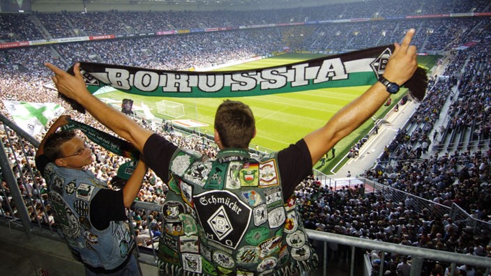 Ein Borussia-Mönchengladbach-Fan hält im Stadion seinen Schal hoch.