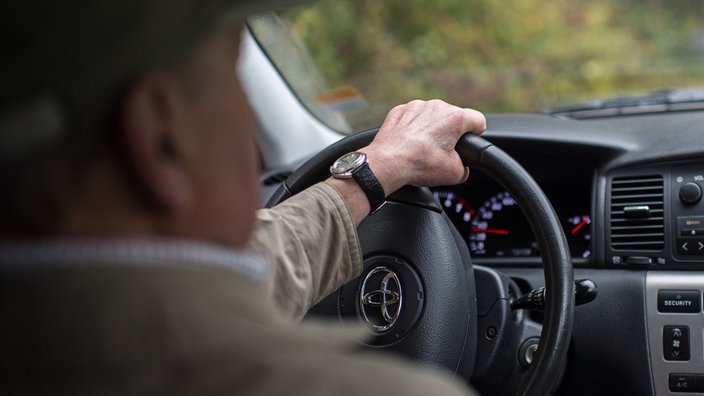 Ein älterer Herr sitzt im Auto und dreht das Lenkrad. | Bildquelle: Wolfram Kastl Ein älterer Herr sitzt im Auto und dreht das Lenkrad.