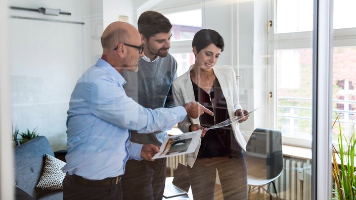 Drei Personen stehen in einem Büro und besprechen einen Ausdruck.