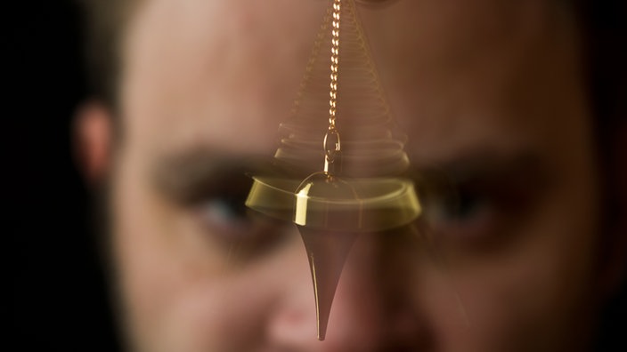 Ein Mann schwingt ein goldenes Pendel | Bildquelle: dpa/Franziska Gabbert Ein Mann schwingt ein goldenes Pendel