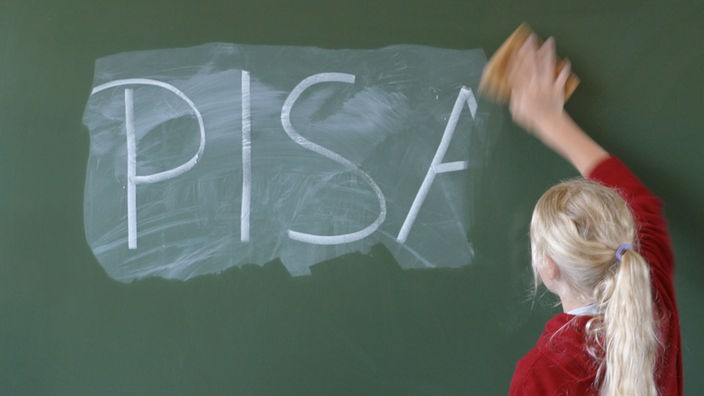 In einer Schule wischt eine Schülerin das Wort "PISA" mit einem Schwamm von der Tafel