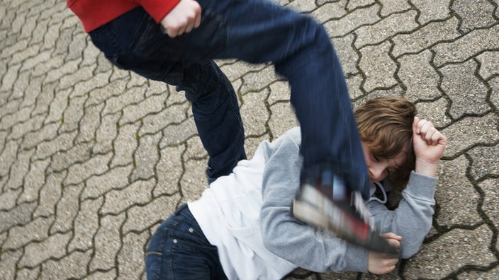 Ein Jugendlicher prügelt auf einen anderen Jungen ein, der am Boden kauert.