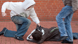 Jugendlicher schlägt auf einen anderen am Boden liegenden Jugendlichen ein, ein zweiter tritt zu