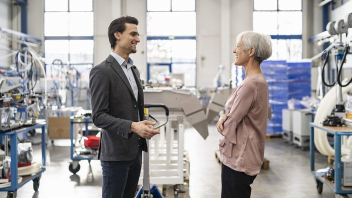 Ein Geschäftsmann und eine Geschäftsfrau lachen miteinander in einer Fabrik