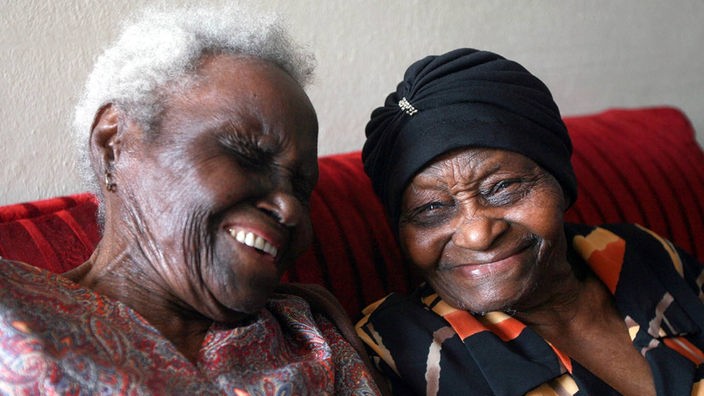 Das Foto zeigt zwei alte, südafrikanische Frauen, die lachen. Es sind Ethel Nembula und Dora Uys an ihrem 100. Geburtstag. Sie sind die ältesten Zwillinge der Welt.