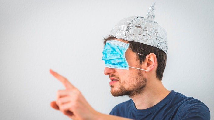 Ein junger Mann mit Aluhut auf dem Kopf und Operationsmaske über den Augen | Bildquelle: picture alliance / Zoonar Ein junger Mann mit Aluhut auf dem Kopf und Operationsmaske über den Augen