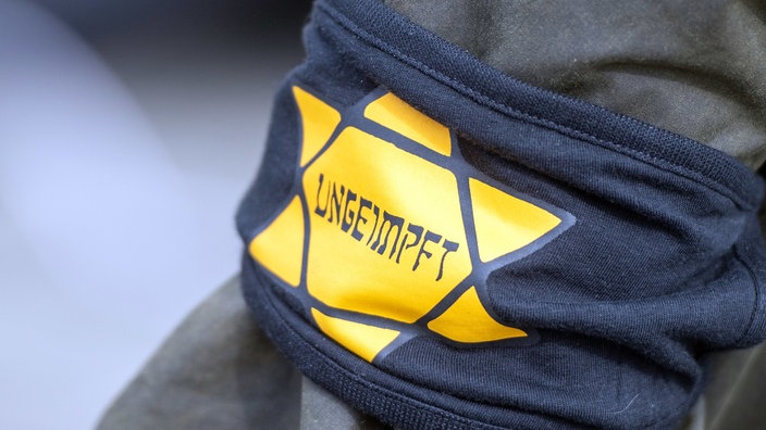 Bei einer Demonstration gegen die Corona-Einschränkungen trägt ein Teilnehmer eine Armbinde mit einem gelben Stern, der an einen Judenstern erinnern soll, mit der Aufschrift "Ungeimpft". | Bildquelle: WDR / dpa Bei einer Demonstration gegen die Corona-Einschränkungen trägt ein Teilnehmer eine Armbinde mit einem gelben Stern, der an einen Judenstern erinnern soll, mit der Aufschrift "Ungeimpft".
