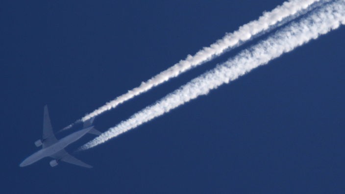 Ein Flugzeug am blauen Himmel mit weißen Kondesstreifen.