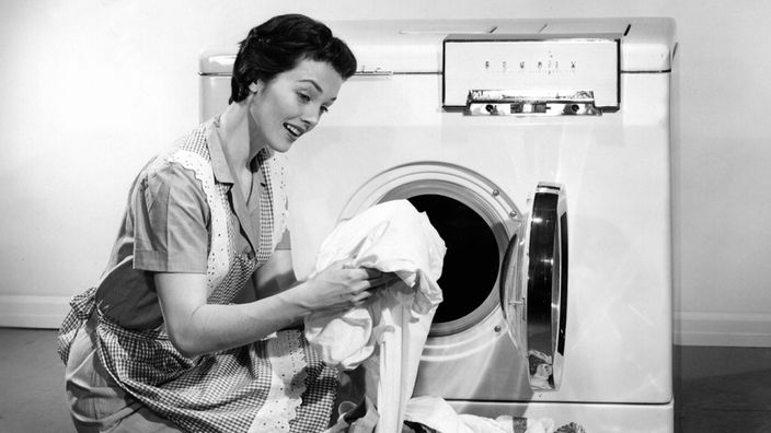 Eine Hausfrau in den 1950er-Jahren befüllt eine Waschmaschine mit Wäsche
