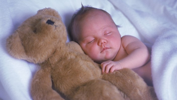 Ein Baby schläft neben einem großen Teddybären.