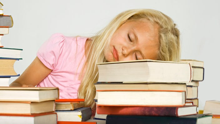 Blondes Mädchen liegt schlafend auf einem Bücherberg.