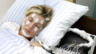 Eine Patientin in einem Schlaflabor. In ihrem Gesicht kleben Elektroden.