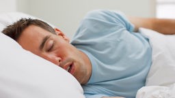 Junger Mann in einem hellen T-Shirt liegt im Bett und schläft