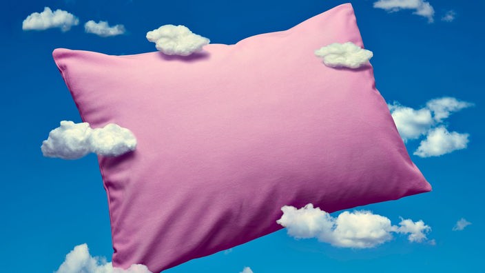 Ein rosa Kissen schwebt vor einem blauen HImmel mit Schäfchenwolken