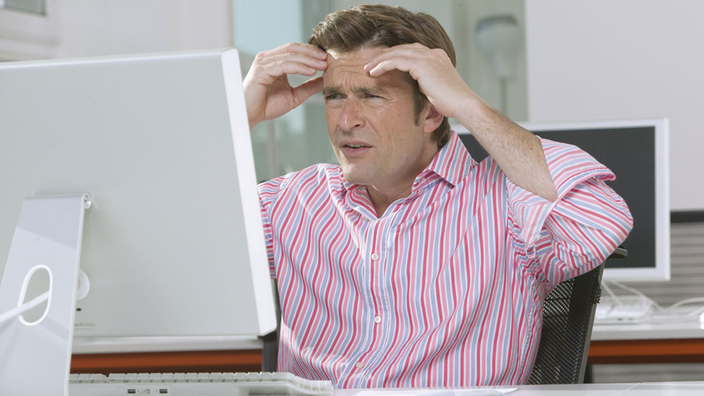 Mann sitzt im Büro gestresst vor Computer
