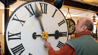 Ein Mann prüft die Beweglichkeit von Zeigern an einem Ziffernblatt einer großen Uhr