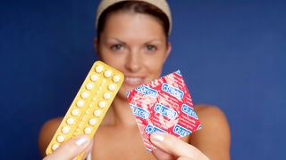 Eine Frau hält die Pille und ein Kondom in den Händen.