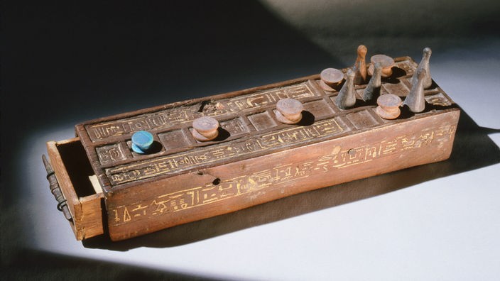 Ein altes ägyptisches Senet-Brettspiel (um 1294-1279 vor Christus) aus Holz, das in Kairo gefunden wurde. Mehrere Spielfiguren stehen auf einer verzierten Holzkiste mit quadratischen Spielfeldern.