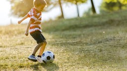 Ein Junge spielt freudig mit einem Ball auf einer Wiese.