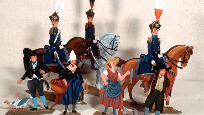 Drei berittene Offiziere in Galauniform des 19. Jahrhunderts, davor Bauersleute in Tracht mit ihren Waren.