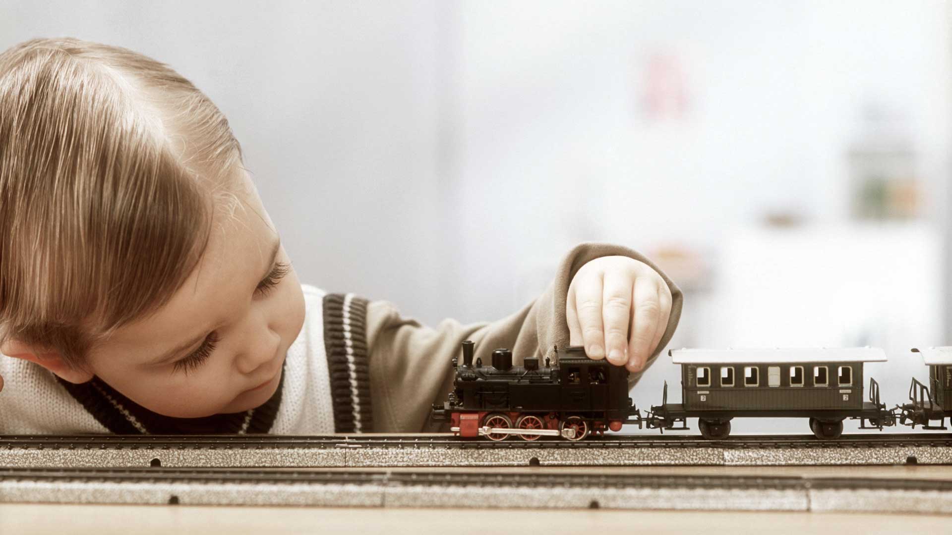 Das alte Foto zeigt einen kleinen Jungen, der mit dem Finger eine Modelleisenbahn berührt.