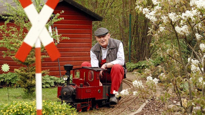 Ein Mann fährt mit einer Modelleisenbahn durch den Garten.