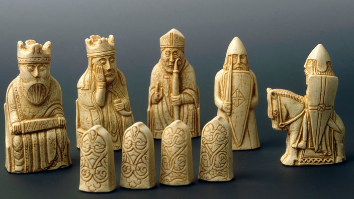 Fünf elfenbeinfarbene norwegische Lewis-Schachfiguren aus Walrossbein: Gesichtszüge und Details wie Krone und Schwert sind filigran herausgearbeitet.