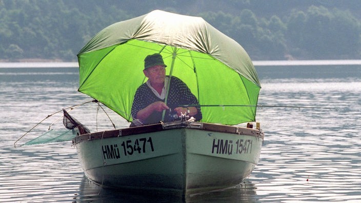 Angler im Boot mit Regenschirm