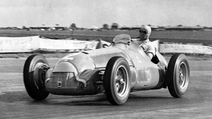 Schwarzweißfoto: Juan Manuel Fangio in einem Rennwagen