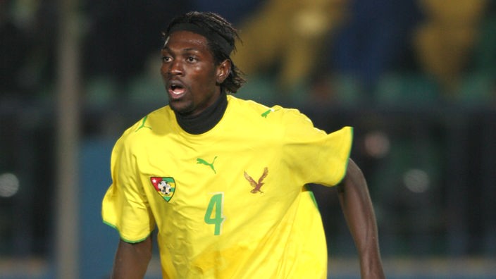 Emmanuel Adebayor in gelbem Trikot und grüner Hose läuft über ein Spielfeld.