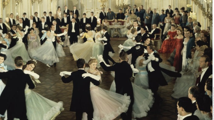 Das Bild zeigt einen historischen Ballsaal, in dem Paare Wiener Walzer tanzen