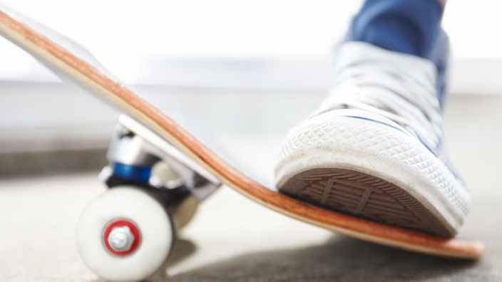 Ein Fuß steht auf dem hinteren Teil des Skateboards.