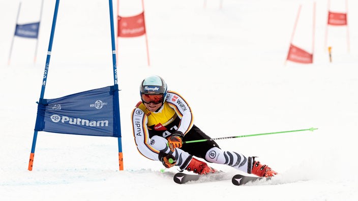 Ein Skiläufer fährt während eines Riesenslamloms ganz eng an einem Slalomtor vorbei.