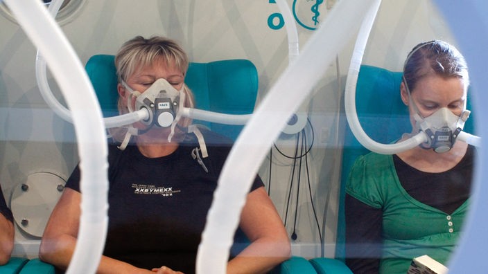 Zwei Frauen sitzen in Dekompressionskammer und inhalieren Sauerstoff.