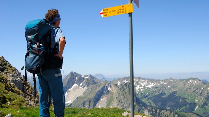 Ein Wanderer steht auf einem Berg an einem Wegweiser.