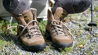 Ein Wanderer hat seine Schuhe ausgezogen, um die Fuesse nach einer Wanderung zu lueften. Seine Füße liegen auf seinen Trekkingschuhen auf