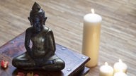 Eine Buddhafigur sitzt auf einer Holzschachtel, daneben brennen Kerzen