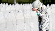 Eine Muslima mit Hijab lehnt an einem weißen Grabstein und trauert