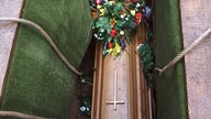 Ein mit Blumen geschmückter Sarg wird in ein Grab hinabgelassen