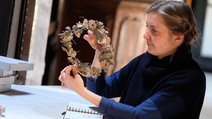 Künstlerin Luzia Werner hält eine alte Totenkrone aus nachgebildeten Blumen in den Händen