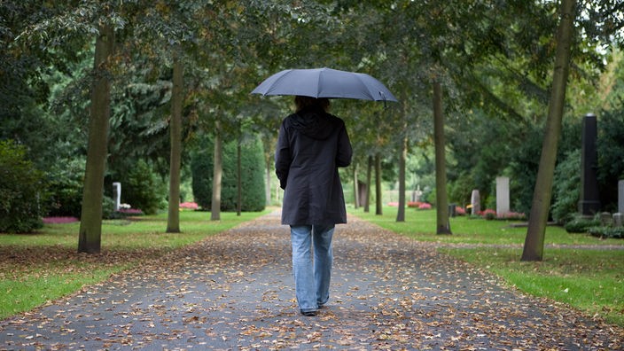 Eine Frau mit Regenschirm auf einem Friedhof