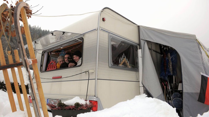 Das Foto zeigt einen Wohnwagen mit Vorzelt im Tiefschnee. Aus dem hinteren Fenster schauen mehrere Menschen heraus und lächeln. | Bildquelle: ddp/Jens-Ulrich Koch Das Foto zeigt einen Wohnwagen mit Vorzelt im Tiefschnee. Aus dem hinteren Fenster schauen mehrere Menschen heraus und lächeln.