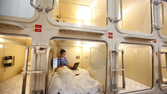 Der Mitarbeiter eines Kapselhotels testet das Bett in einer viereckigen, weißen Plastikröhre - einem Hotelzimmer.