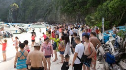 Eine große Anzahl von Touristen an einem weißen Sandstrand.