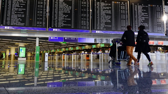 Zwei Reisende gehen an einer Flughafen-Anzeigentafel vorbei. | Bildquelle: imago images/Frank Sorge Zwei Reisende gehen an einer Flughafen-Anzeigentafel vorbei.