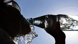 Eine junge Frau erfrischt sich mit einem Schluck aus einer Flasche Mineralwasser.