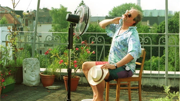 Mann sitzt auf einem Balkon vor einem Ventilator