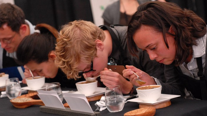 Vier junge Menschen beugen sich über die Tassen und riechen am Kaffee.