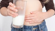 Groißaufnahme: Ein Mädchen fasst sich an den Bauch und hält in der anderen Hand ein Glas Milch