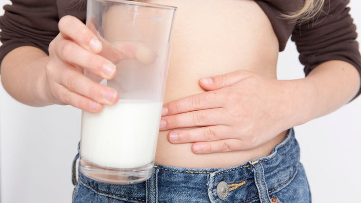 Groißaufnahme: Ein Mädchen fasst sich an den Bauch und hält in der anderen Hand ein Glas Milch